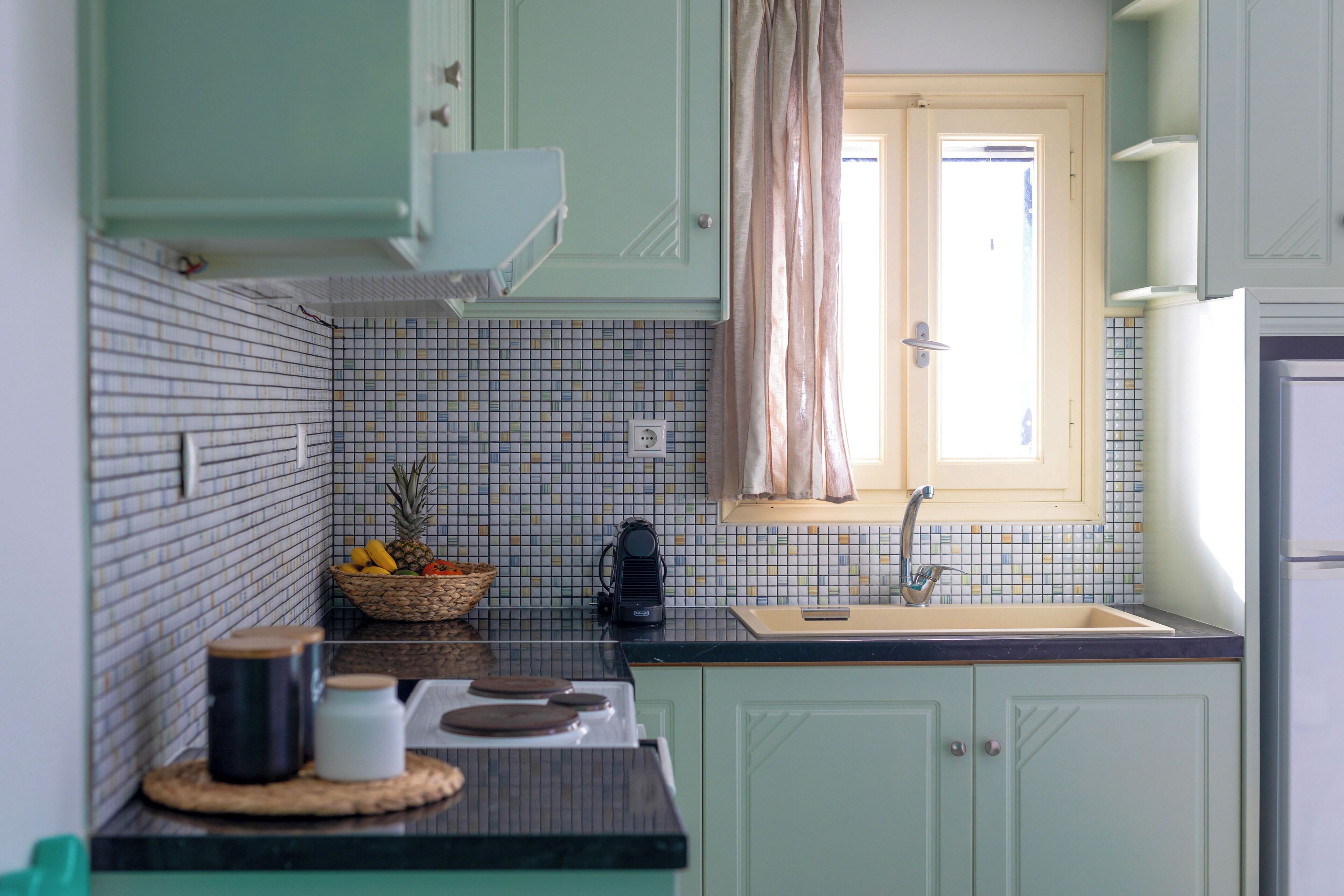 A kitchen with a tiled backsplash, a window with curtains, and a sink.