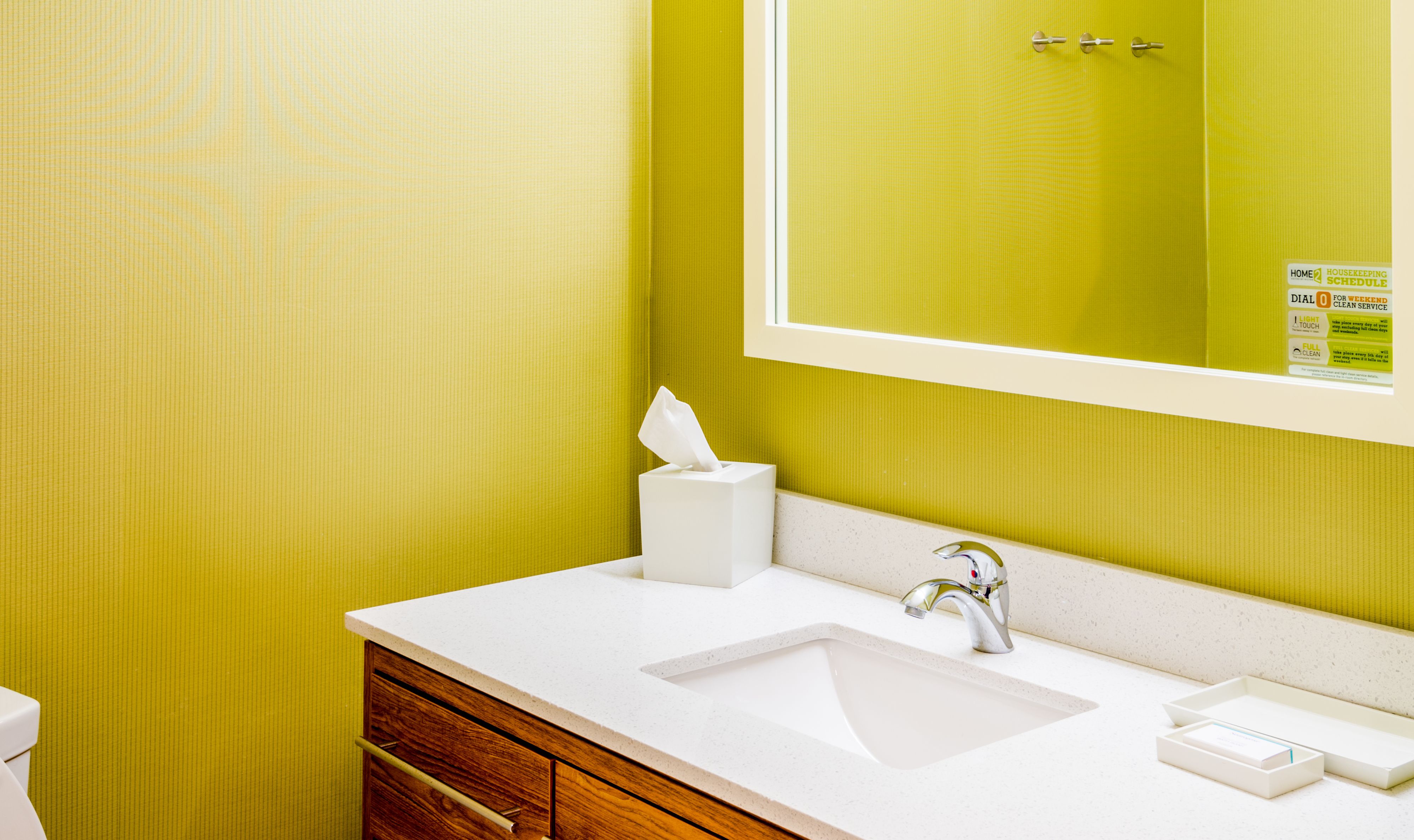 Une salle de bain avec un lavabo blanc, un meuble en bois et un miroir devant un mur vert.