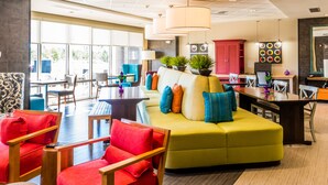 Un hall d’hôtel moderne avec un canapé jaune, des fauteuils rouges et un coin repas agrémenté d’un buffet rouge.