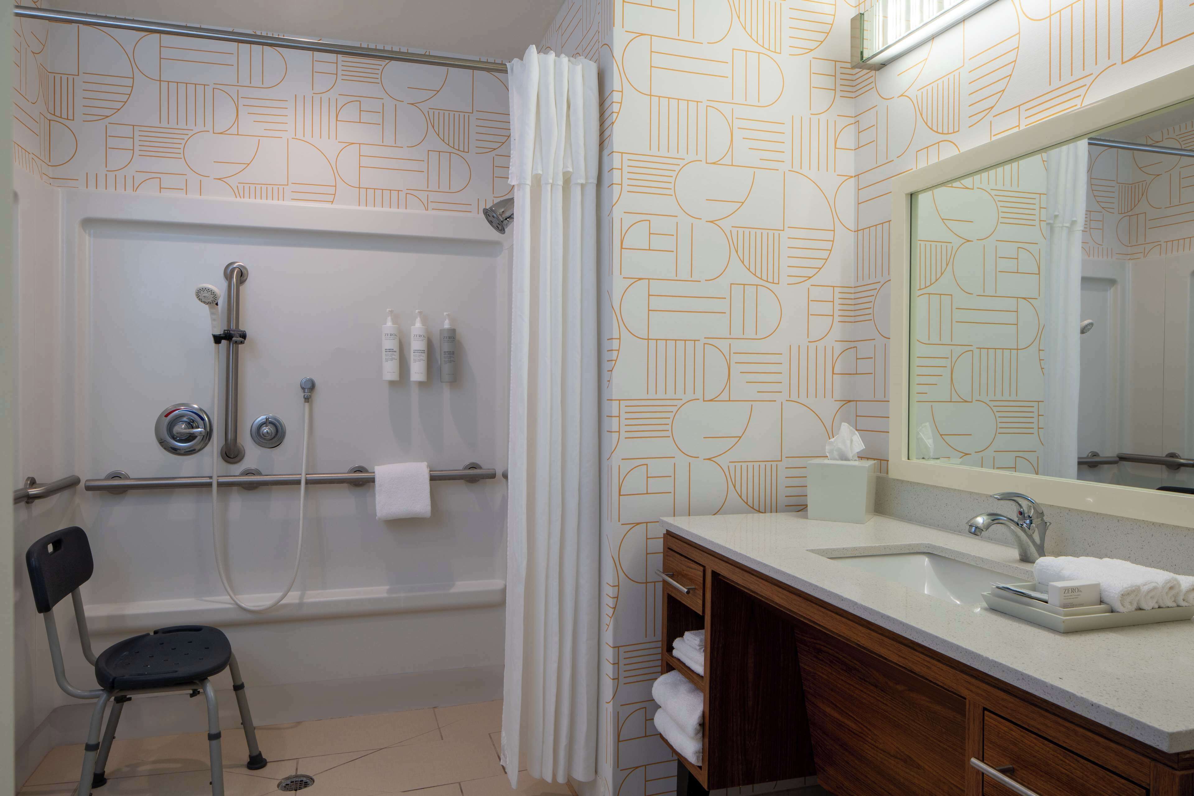 Un bagno con doccia, lavandino, specchio e una sedia.