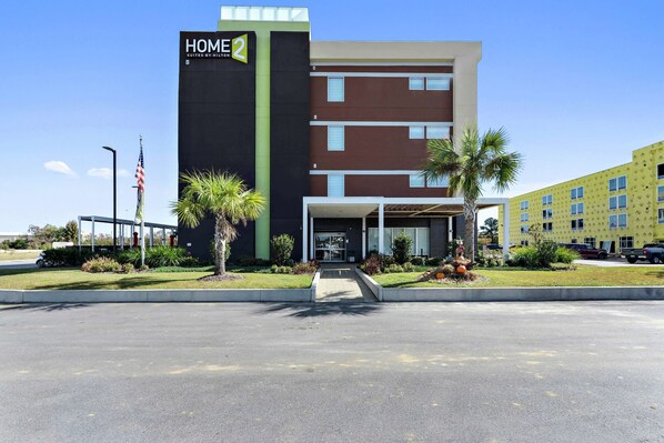 A modern hotel with a prominent "HOME 2" sign, a covered entrance, and a parking lot. - Home2 Suites by Hilton Gulfport I-10 (Gulfport)