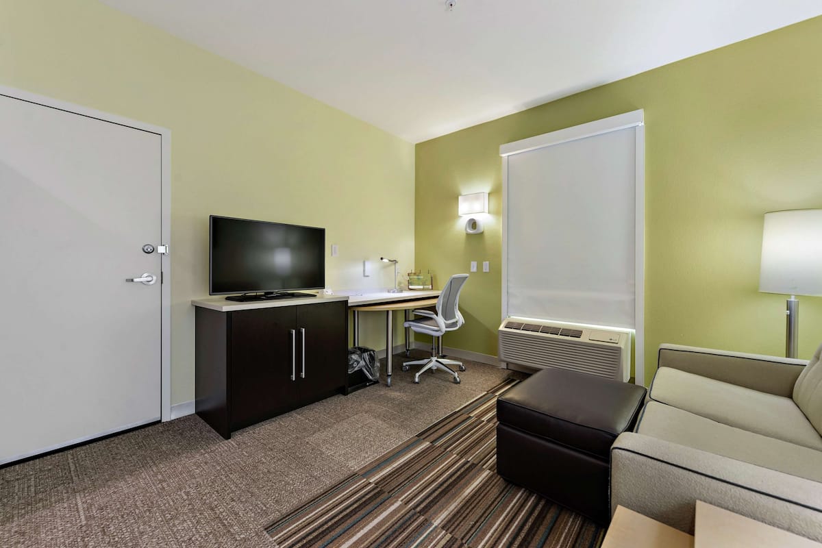 Hotellihuone, jossa on työpöytä, televisio, toimistotuoli ja sohva.