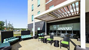Un espace extérieur aménagé en terrasse, avec des meubles en osier, un coin salon couvert et une vue sur la façade du bâtiment.