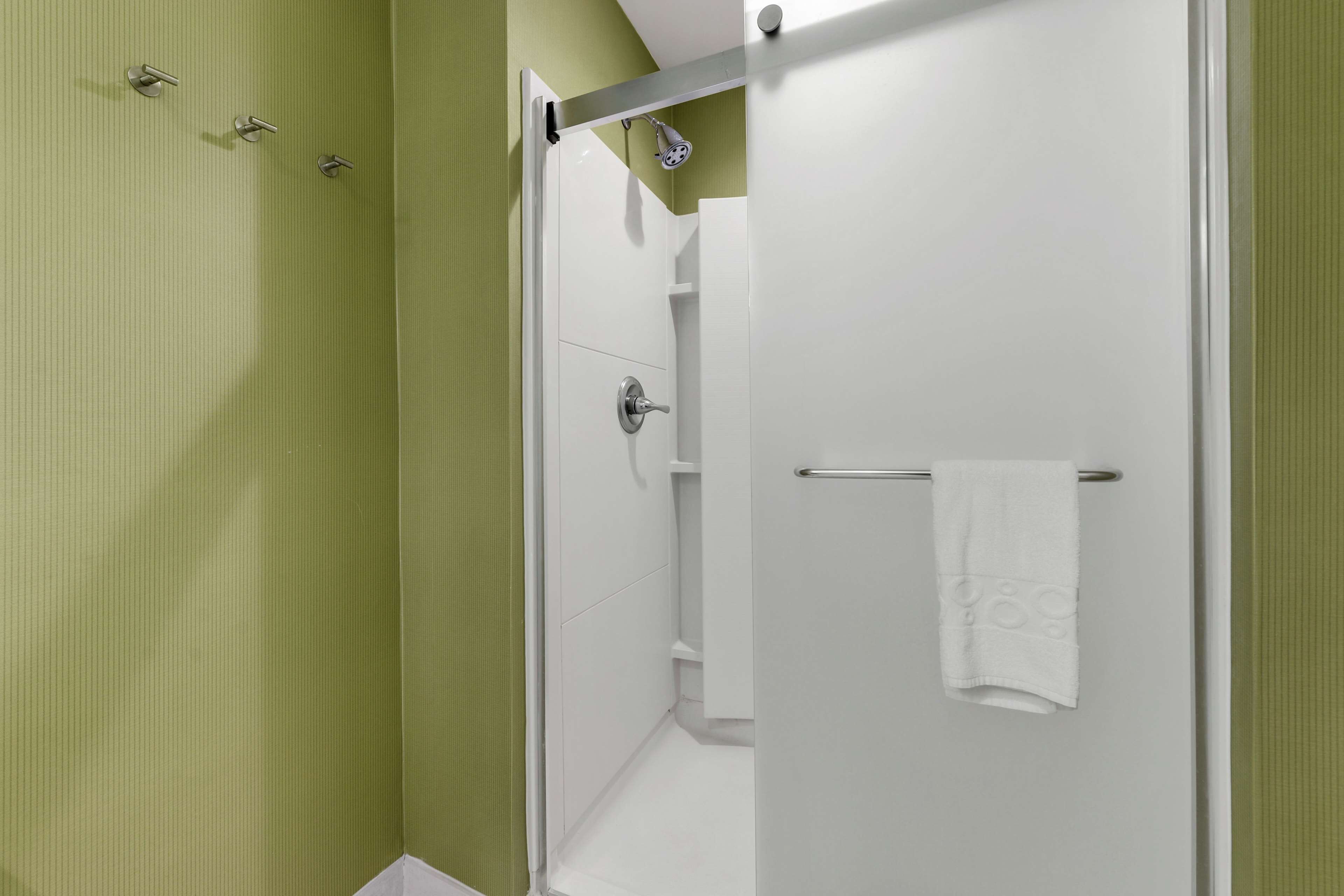 Un baño moderno con cabina de ducha de vidrio, una toalla blanca colgada en la puerta y una pared verde.