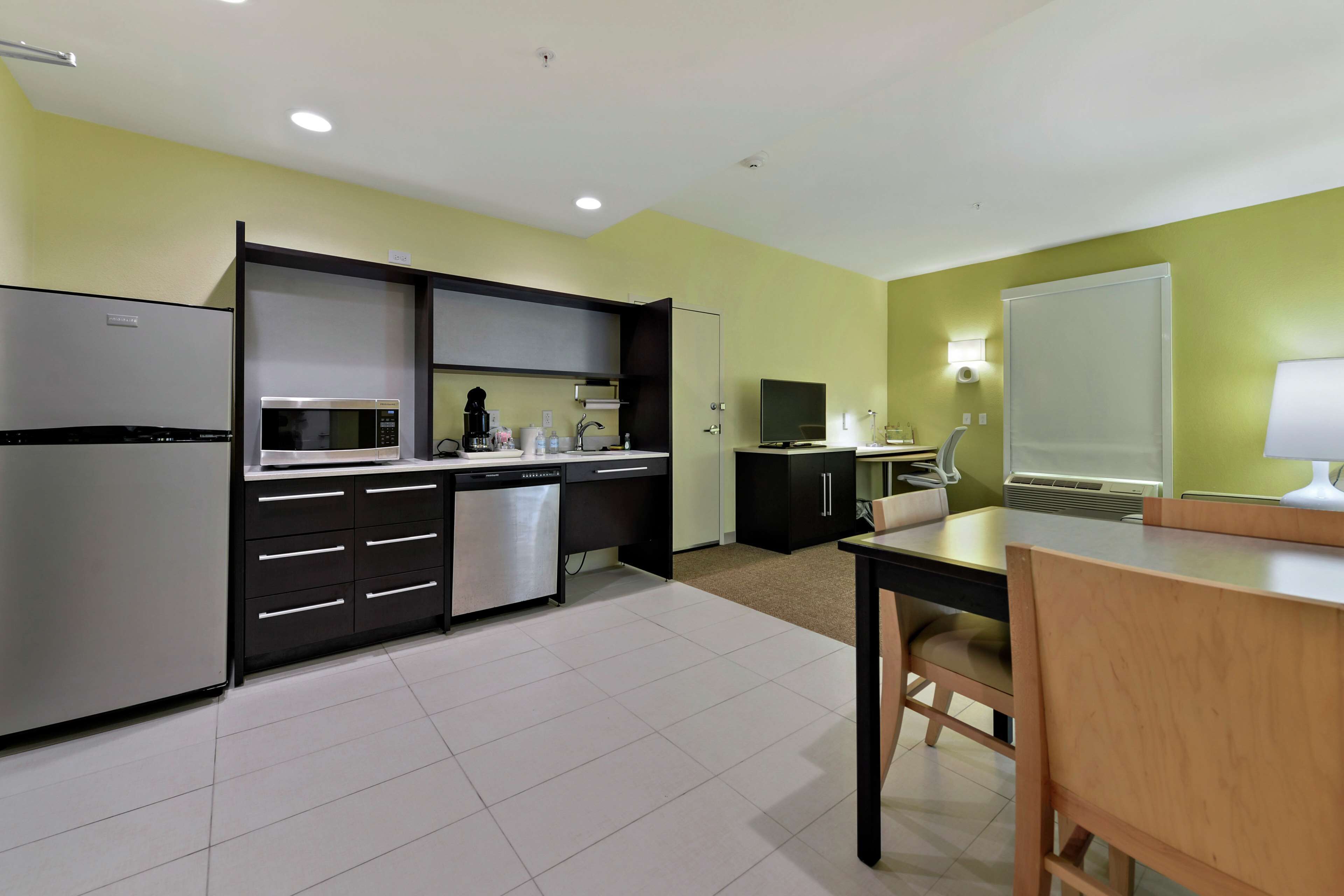 Una cocina moderna con refrigerador, microondas y lavavajillas. Hay una mesa de comedor con sillas y un televisor sobre un mueble.