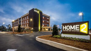 Un hôtel moderne, facilement reconnaissable à son enseigne bien visible « HOME 2 Suites by Hilton », qui se distingue par son bâtiment à plusieurs étages, doté d’un toit plat et d’une entrée bien éclairée.