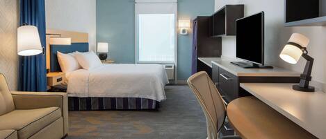 A hotel room with a bed, a desk with a computer, a chair, a sofa, and a TV.