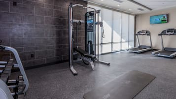 A modern gym with a pull-up bar, weight bench, treadmills, and a large window providing natural light.