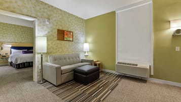 A hotel room with a sofa, ottoman, and a bed in the background.