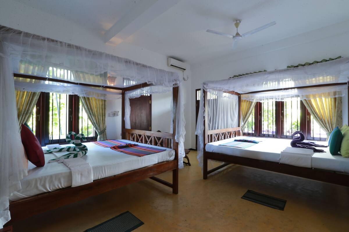 Two wooden beds with white bedding and mosquito netting, a ceiling fan, and a window with curtains.