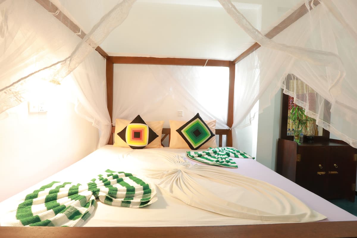 A bed with a canopy, pillows with geometric patterns, and a bedside table with a vase.