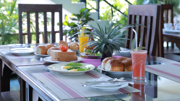A dining table set with plates of food, including bread, a fruit salad, and a glass of juice. - Hotel Baywatch (Unawatuna)