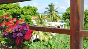 A balcony with a view of a tropical garden and the ocean. - Hotel Baywatch (Unawatuna)