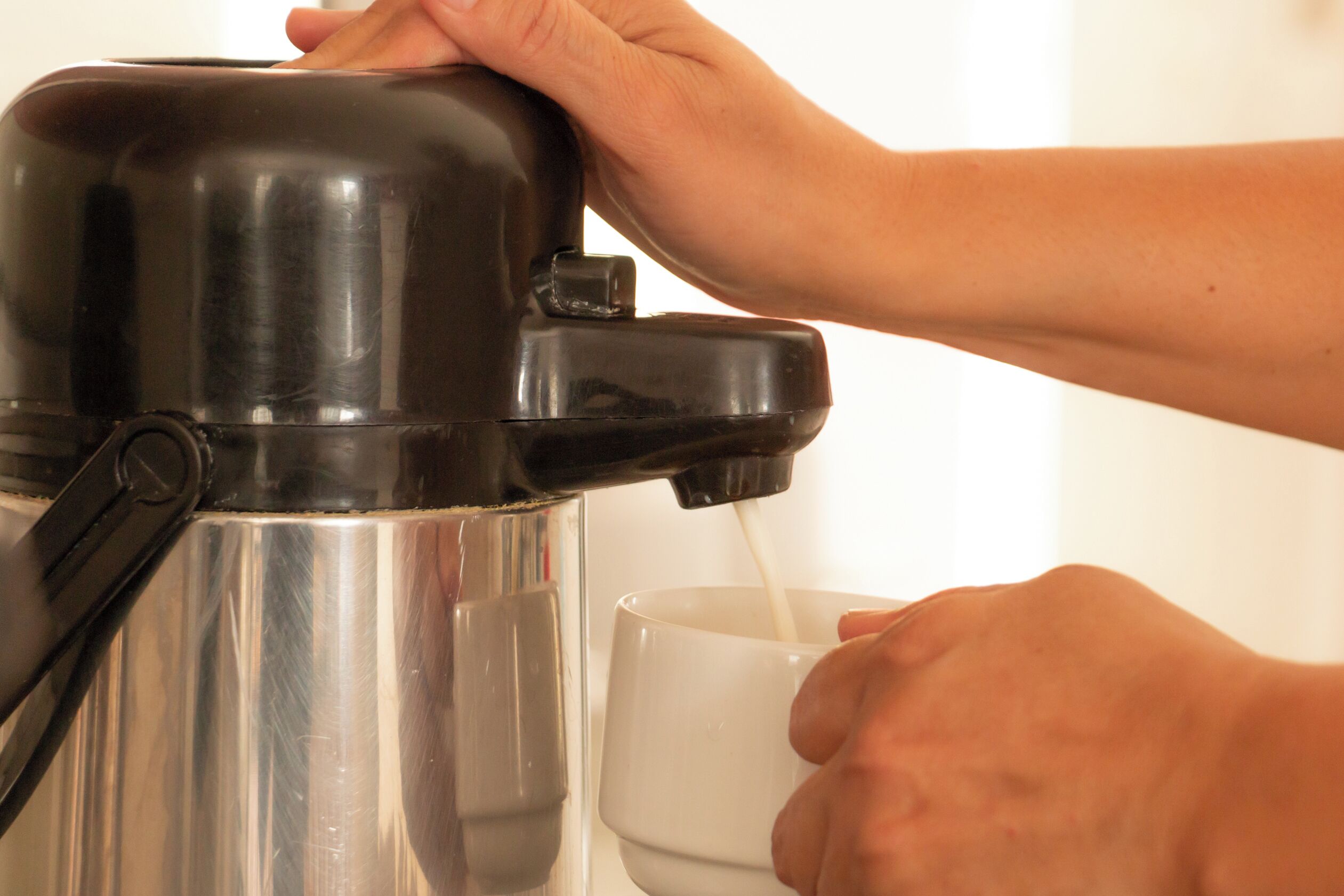 Iemand giet vloeistof uit een koffiezetapparaat in een kop.