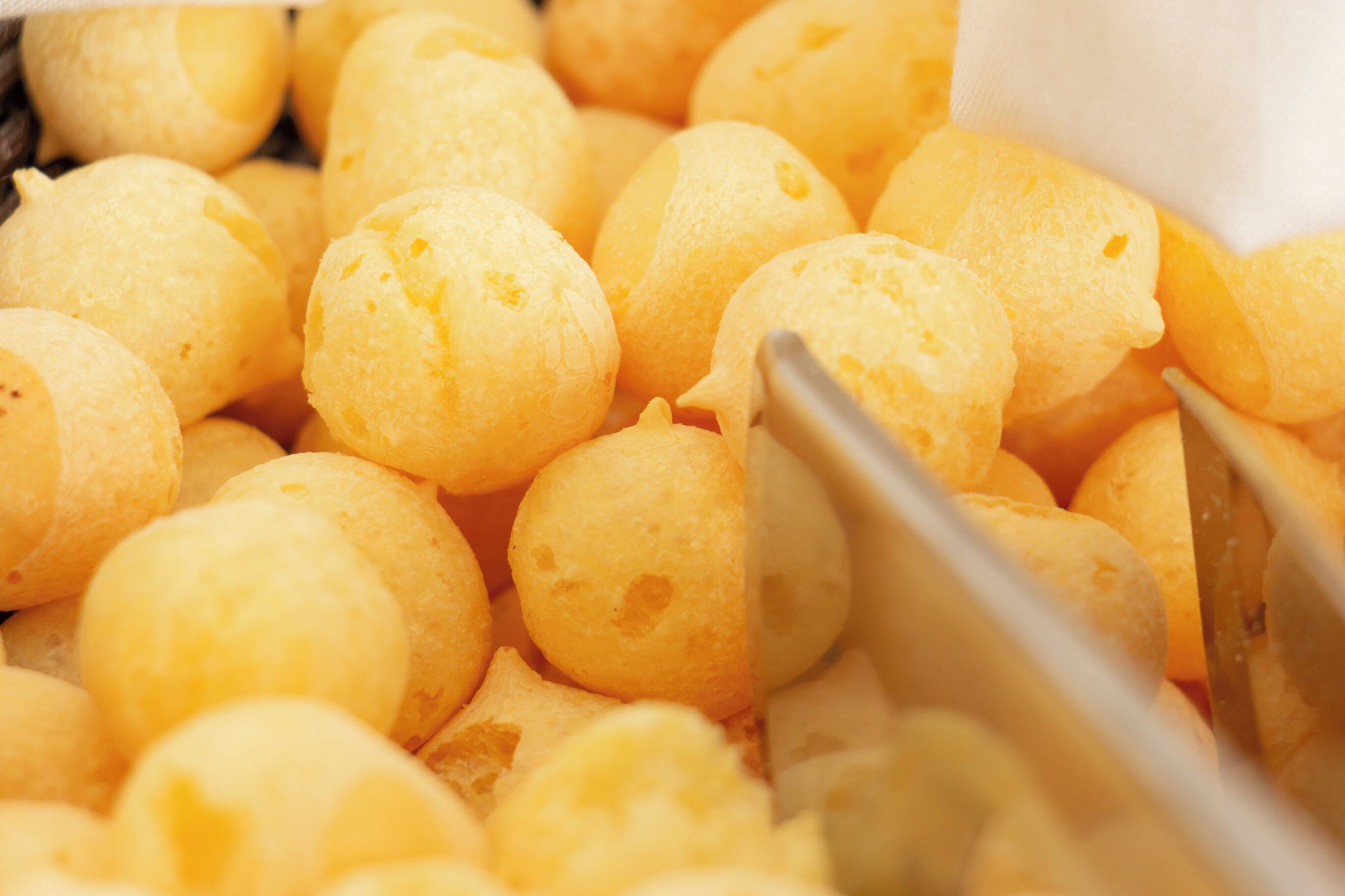 Lähikuva keltaisista, pyöreistä ja pinnaltaan kuvioiduista elintarvikkeista, todennäköisesti jonkinlainen leipä tai leivonnainen, ja kuvassa on osittain näkyvissä jokin keittiöväline.