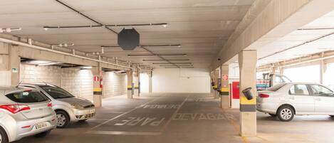 A parking garage with concrete pillars, marked parking spaces, and two parked cars.