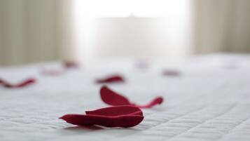 Cama com colcha branca e pétalas de rosa espalhadas.