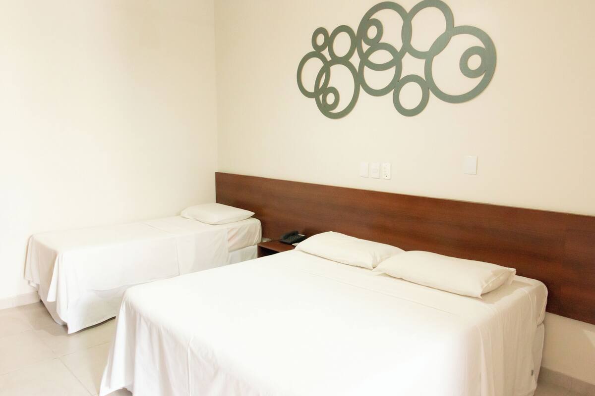 A hotel room with two single beds, a wooden headboard, a wall-mounted phone, and a decorative wall piece.