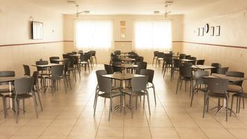 Un comedor amplio con varias mesas y sillas, ventanas grandes con cortinas y ventiladores de techo.