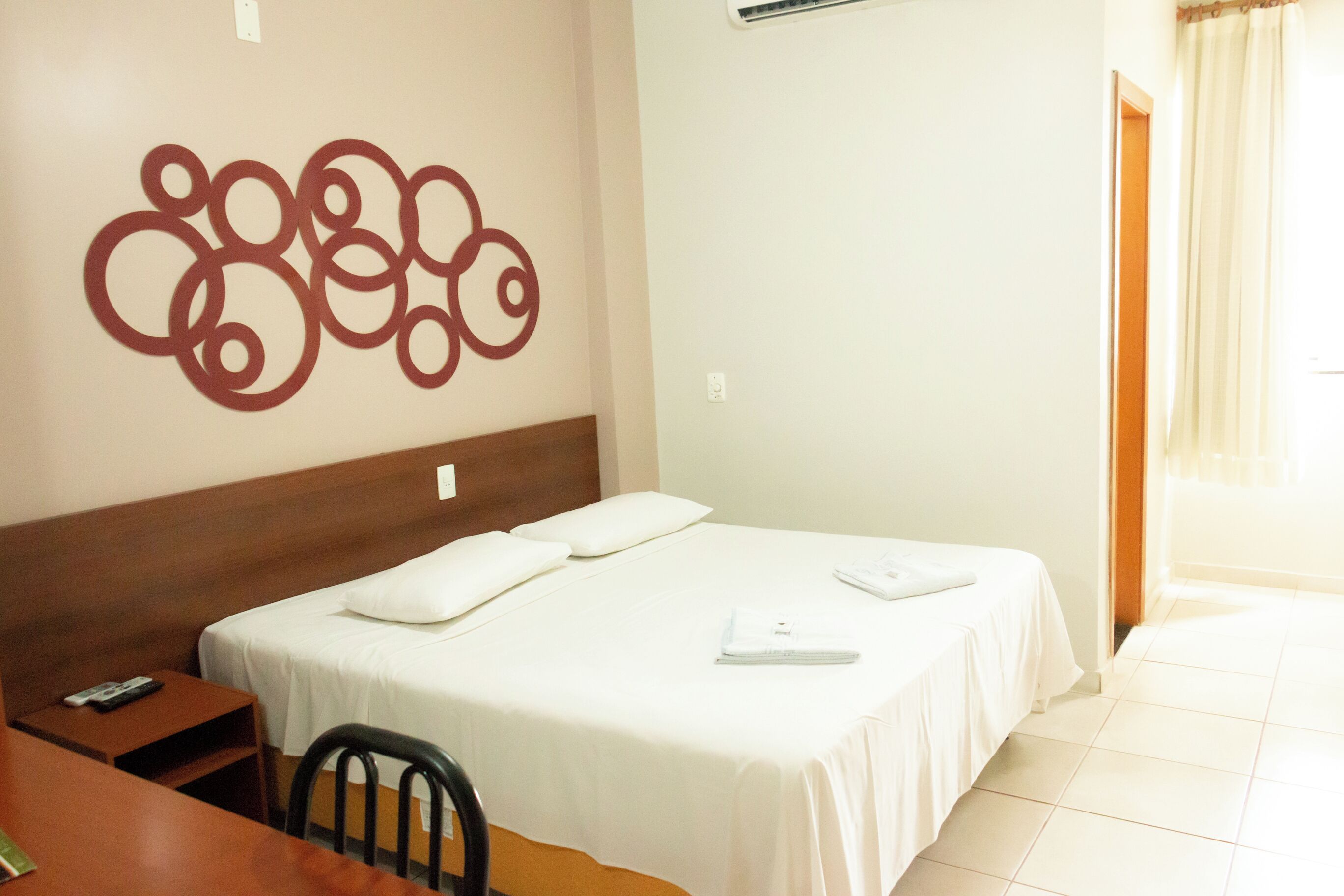 A hotel room with a bed, a desk, a chair, and a wall decoration.