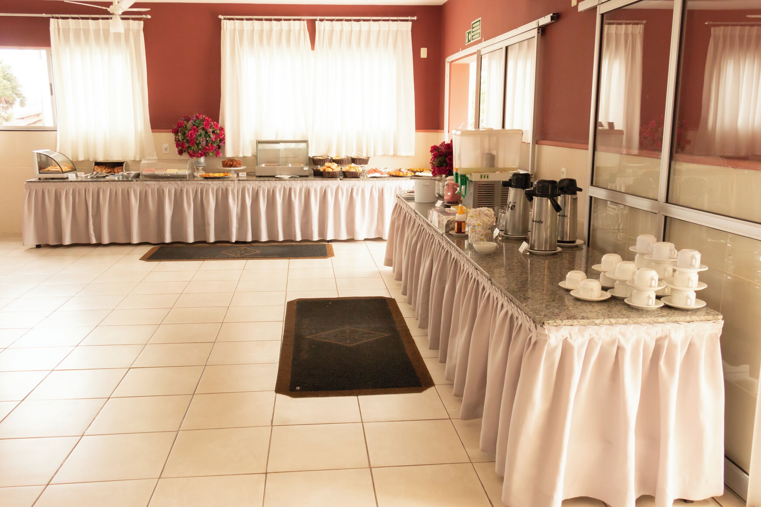 Montaje tipo bufé con diversos alimentos y bebidas, una estación de café y una zona de estar con vistas al exterior.