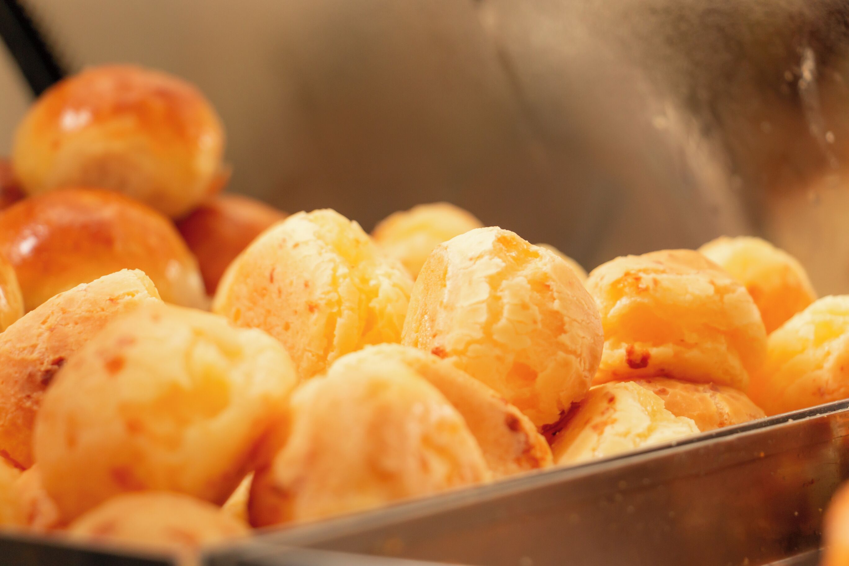 Uma bandeja com doces folhados dourados, provavelmente croissants ou produtos de panificação semelhantes, em um recipiente de metal.