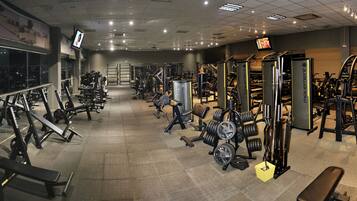 Un gimnasio con varios equipos de ejercicio, incluyendo bancos, máquinas de pesas y pesas sueltas.