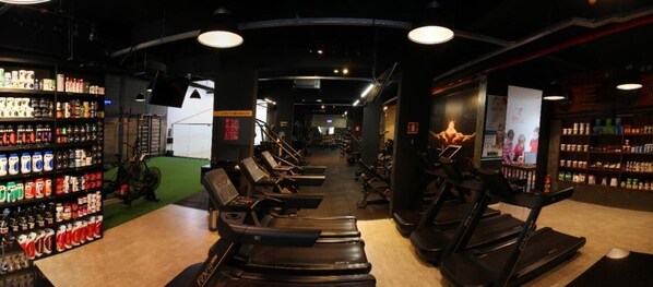 Een sportschool met loopbanden, hometrainers en een muur vol fitnesssupplementen.