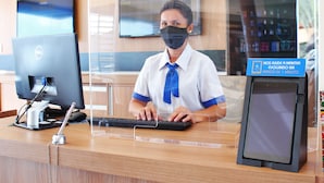 A reception desk with a computer, a phone, and a sign indicating assistance within 1 minute. - Bernal Hotel Econômico (Ituiutaba)