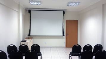 Una sala de conferències amb pantalla de projector, cadires negres, pissarra i una porta.