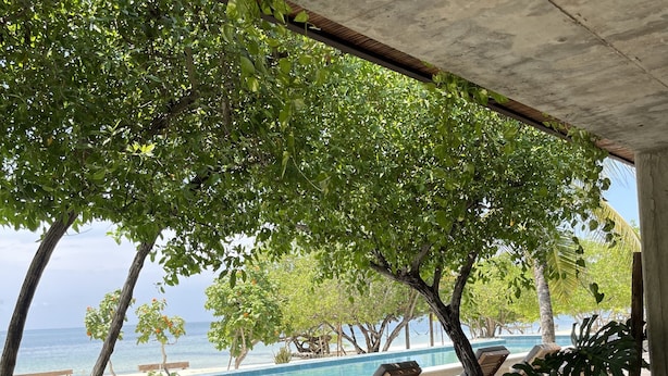 A covered outdoor seating area with wooden tables and chairs, overlooking a pool and the ocean. - SABAI (Cartagena)