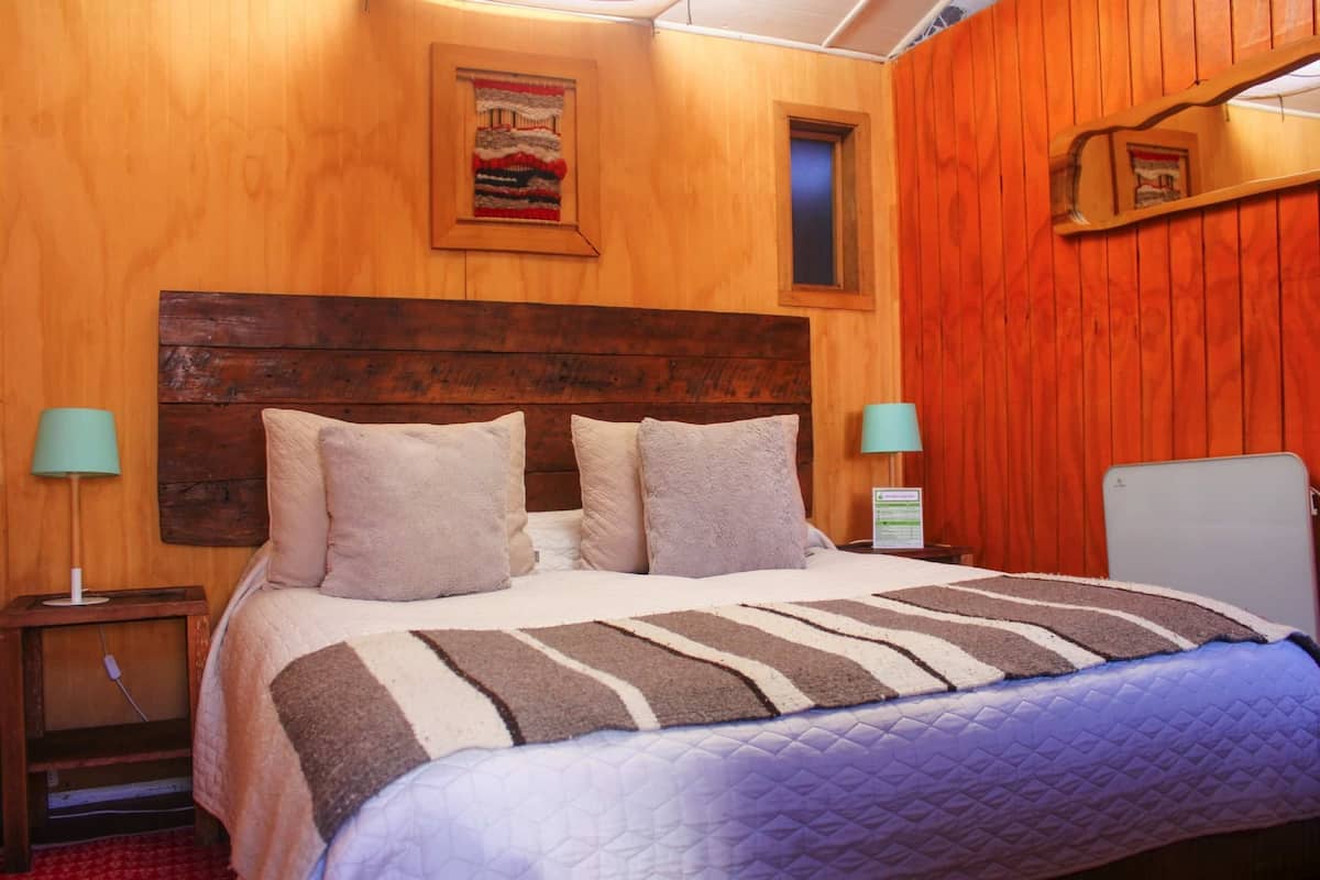 A wooden-paneled room with a bed, two bedside tables, and a nightstand.
