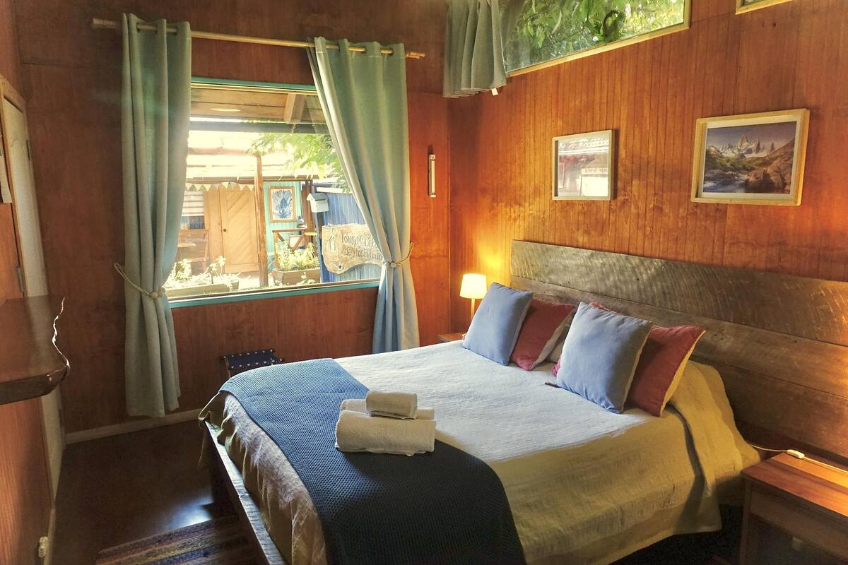 A hotel room with a wooden headboard, a bed with a blue and white bedspread, two pillows, and a bedside table with a lamp.