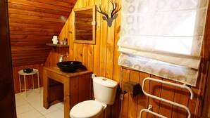 Baño de cabaña de madera con inodoro, lavamanos y ventana con cortinas estampadas.