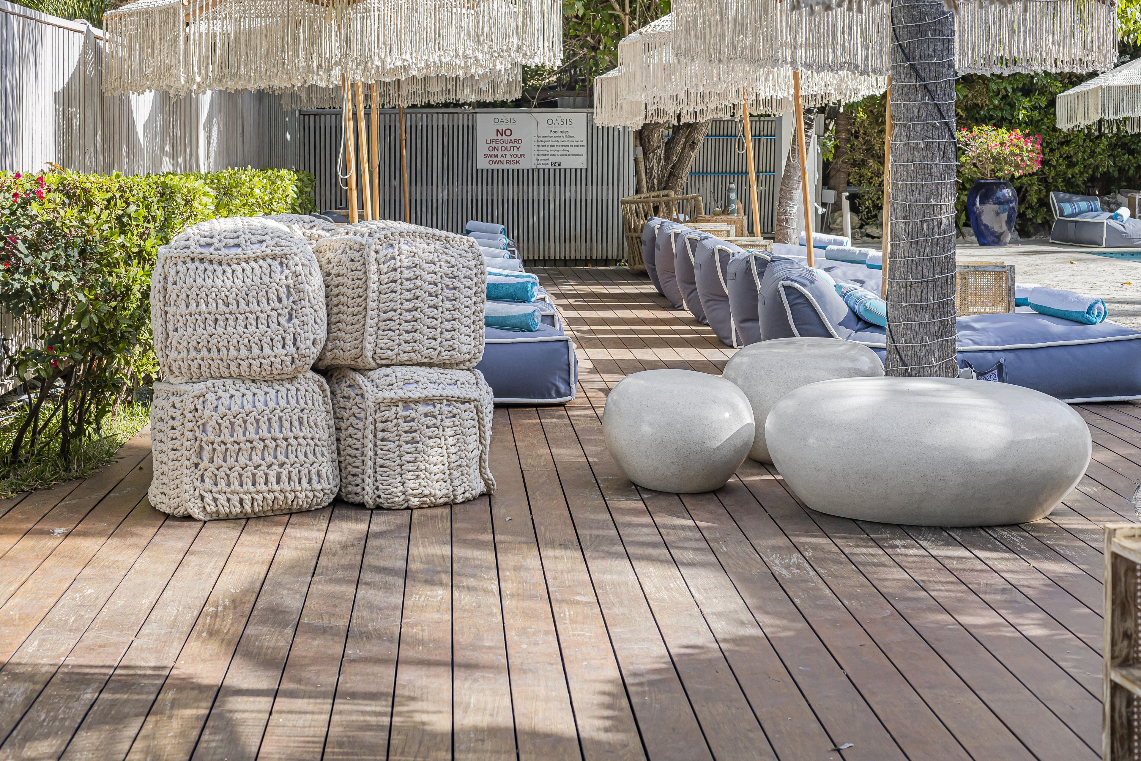 A wooden deck with outdoor seating, including round and rectangular cushions, and a sign indicating a lifeguard on duty.