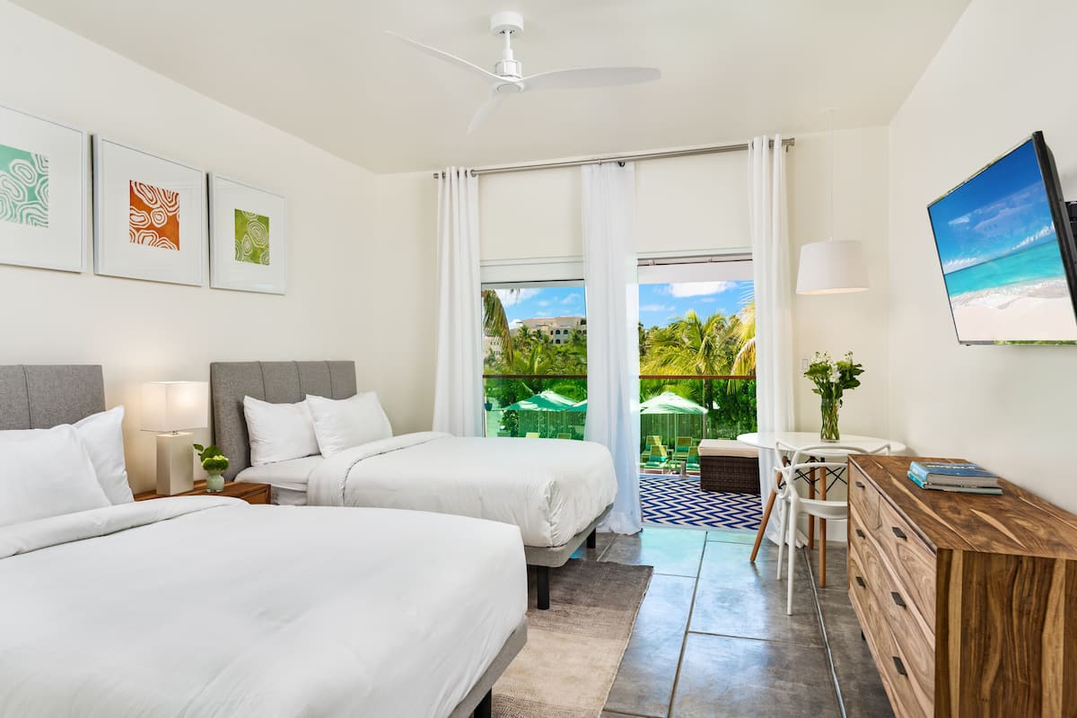 Ein Hotelzimmer mit zwei Betten, einem Schreibtisch, einem Fernseher und einem Balkon mit Blick auf den Strand.