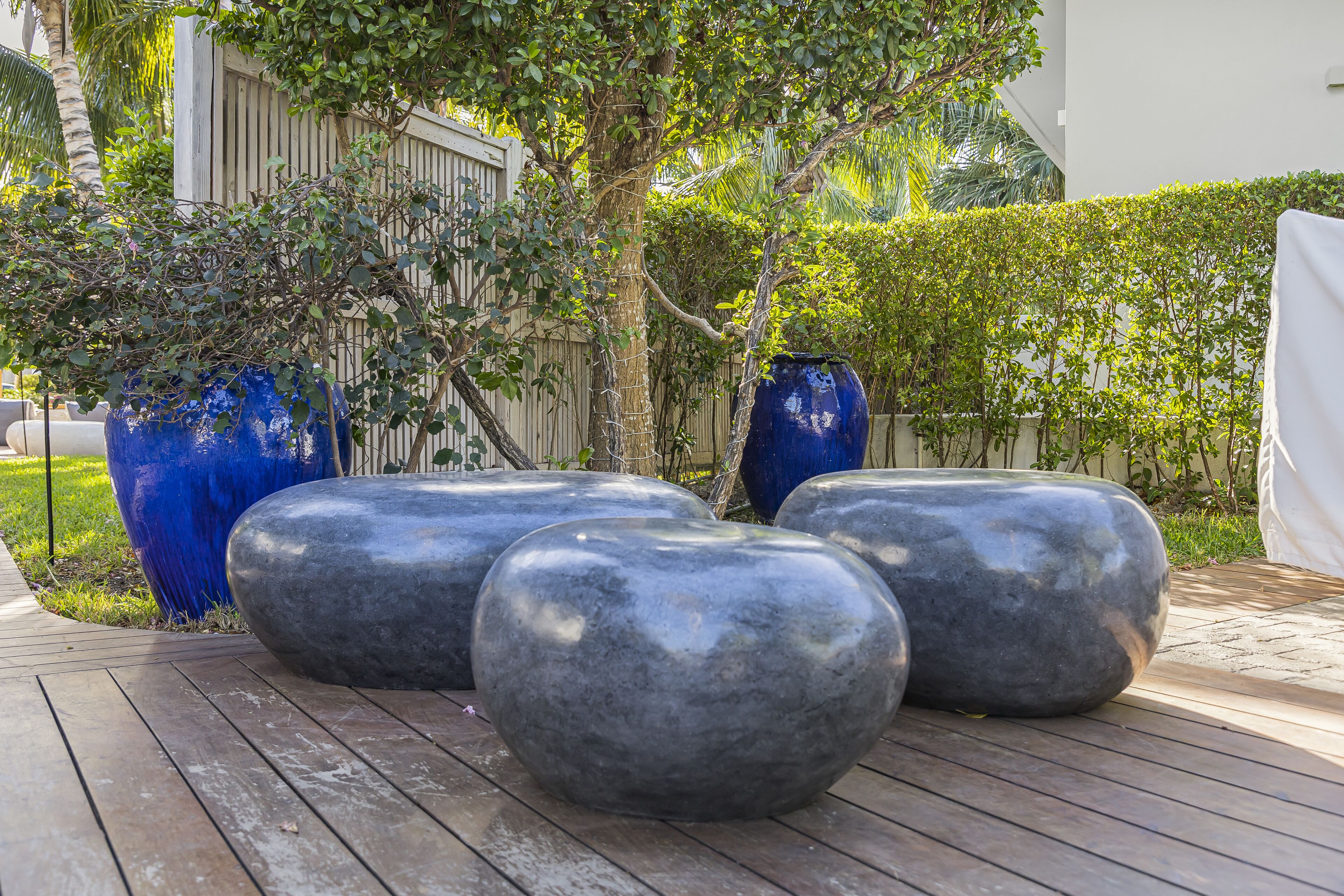 A wooden deck with large, smooth, gray planters and a blue vase.