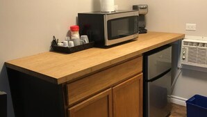 A compact kitchen with a microwave, a small refrigerator, and a wooden countertop.