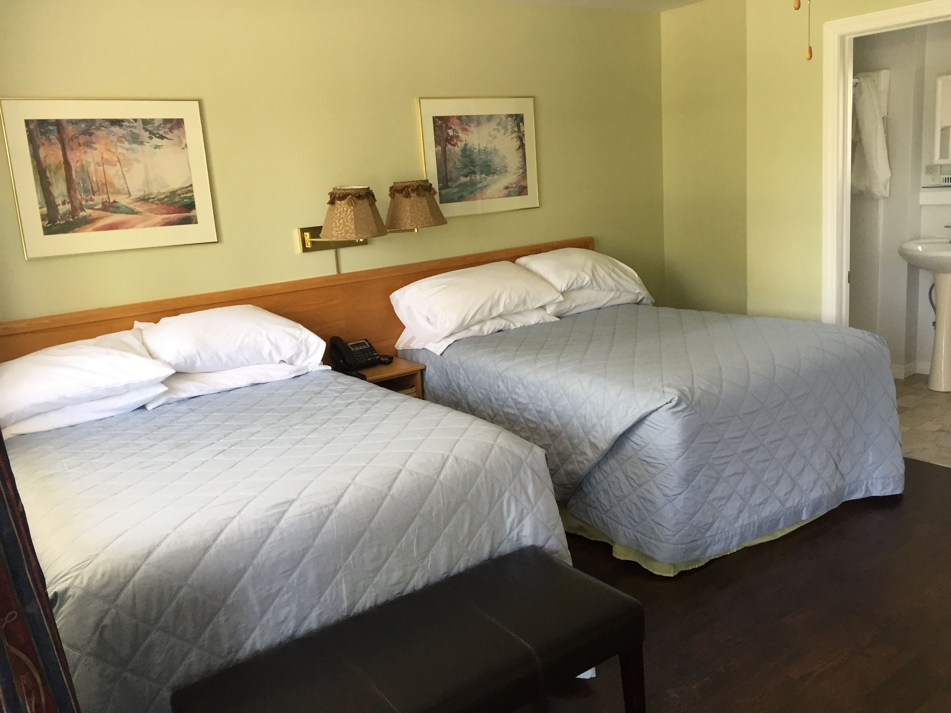 A hotel room with two beds, a bedside table with a phone, and two paintings on the wall.