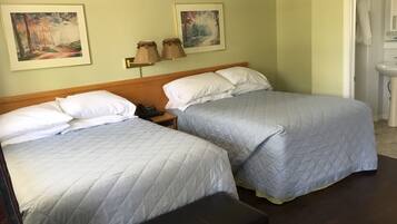 A hotel room with two beds, a bedside table with a phone, and two paintings on the wall.