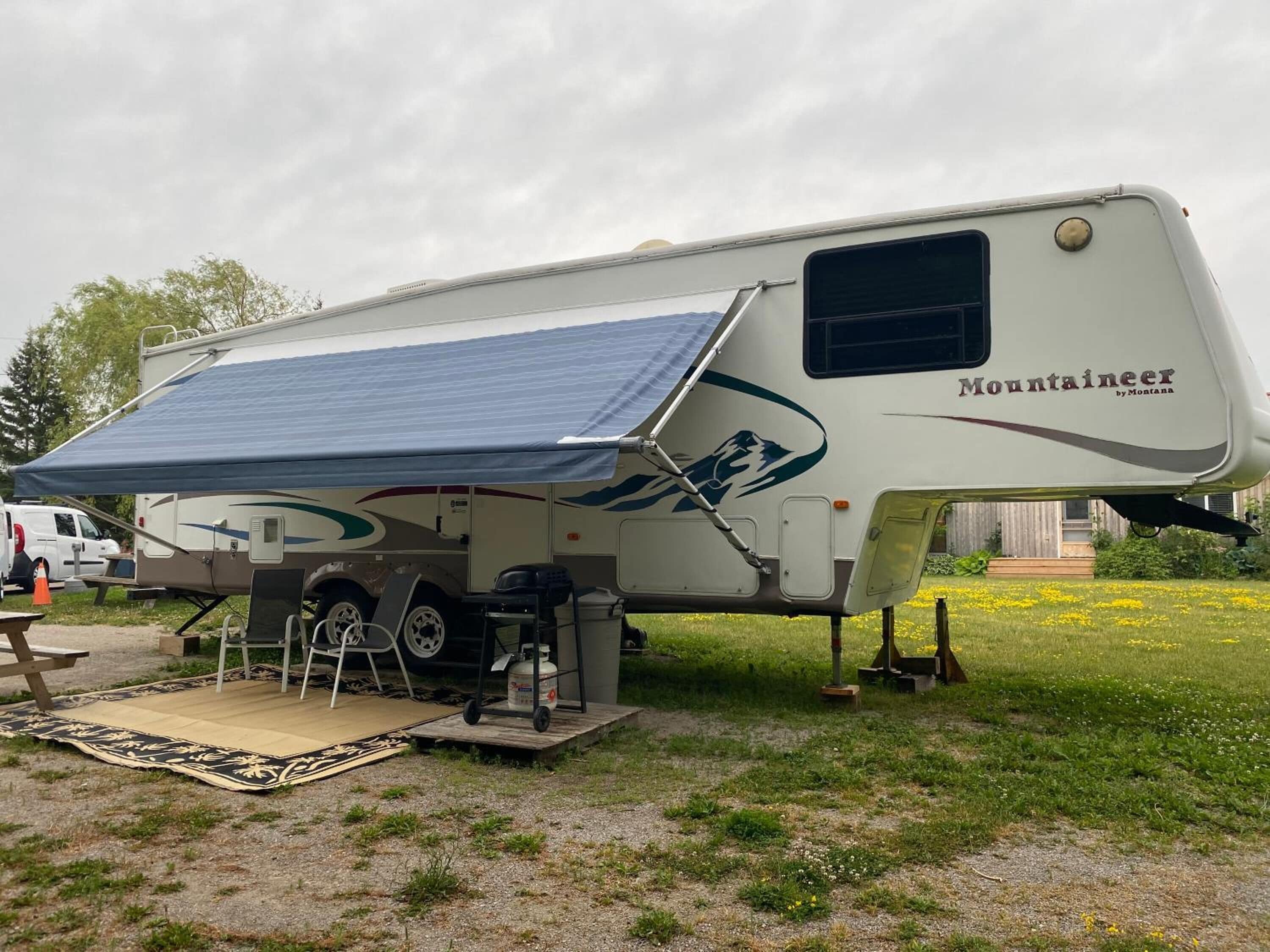 Una gran autocaravana con toldo cubierto, zona de cocina y pequeño espacio para sentarse al aire libre.
