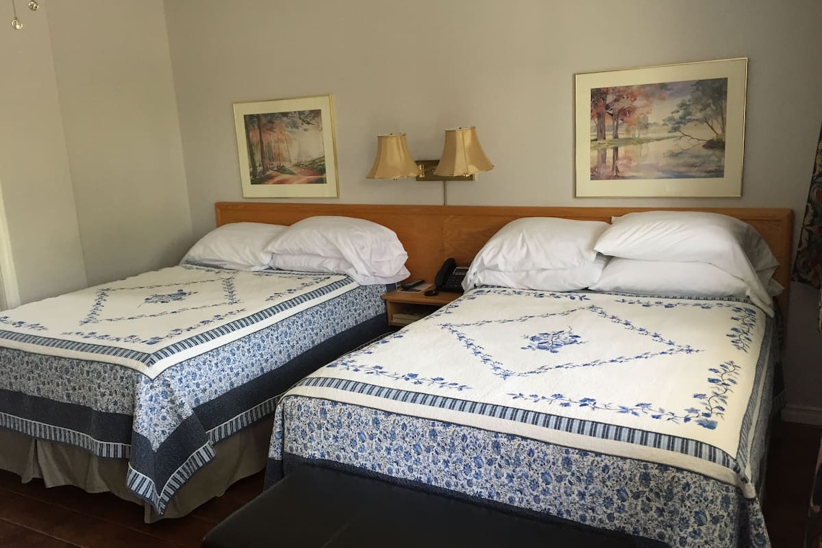 A hotel room with two single beds, each with a floral bedspread and white pillows. There are two wall-mounted lamps and two framed paintings above the beds.