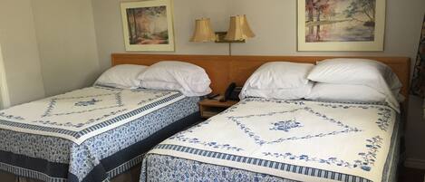 A hotel room with two single beds, each with a floral bedspread and white pillows. There are two wall-mounted lamps and two framed paintings above the beds.