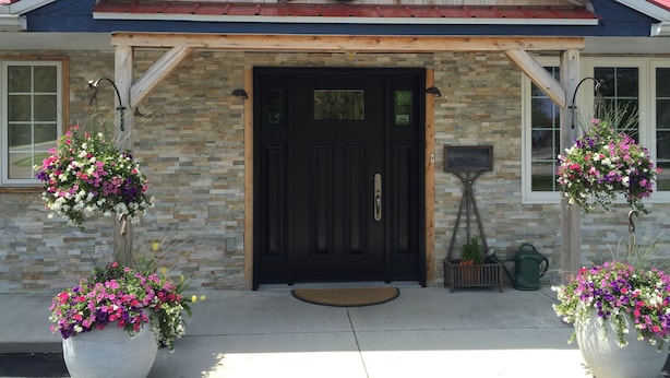 A house with a stone facade, a black front door, and two large flower planters on either side.