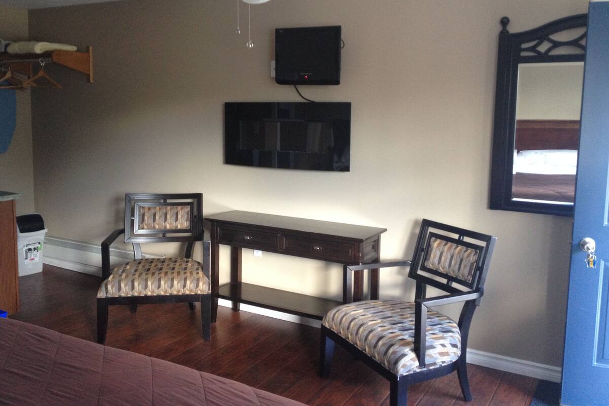 A room with a ceiling fan, a TV mounted on the wall, a wooden desk, two chairs, and a door.