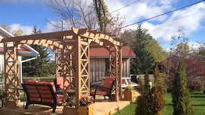 A wooden pergola with seating, surrounded by a well-maintained lawn and trees.