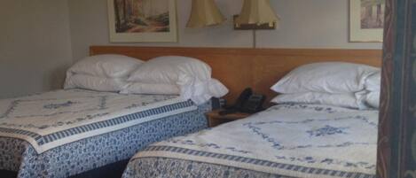 A hotel room with two beds, each with a patterned bedspread, a wooden headboard, a bedside table with a lamp, and a phone.
