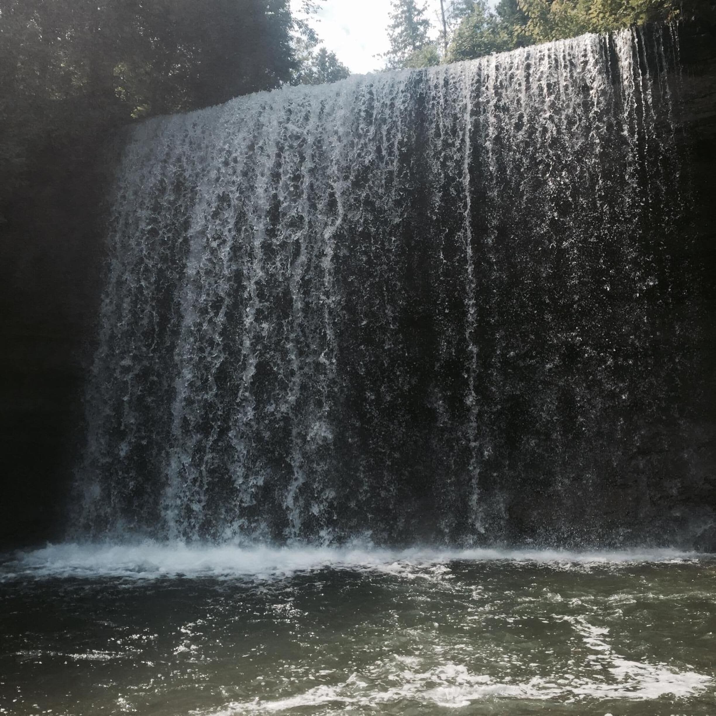 Una cascada se precipita por un risco rocoso hacia una poza de agua.