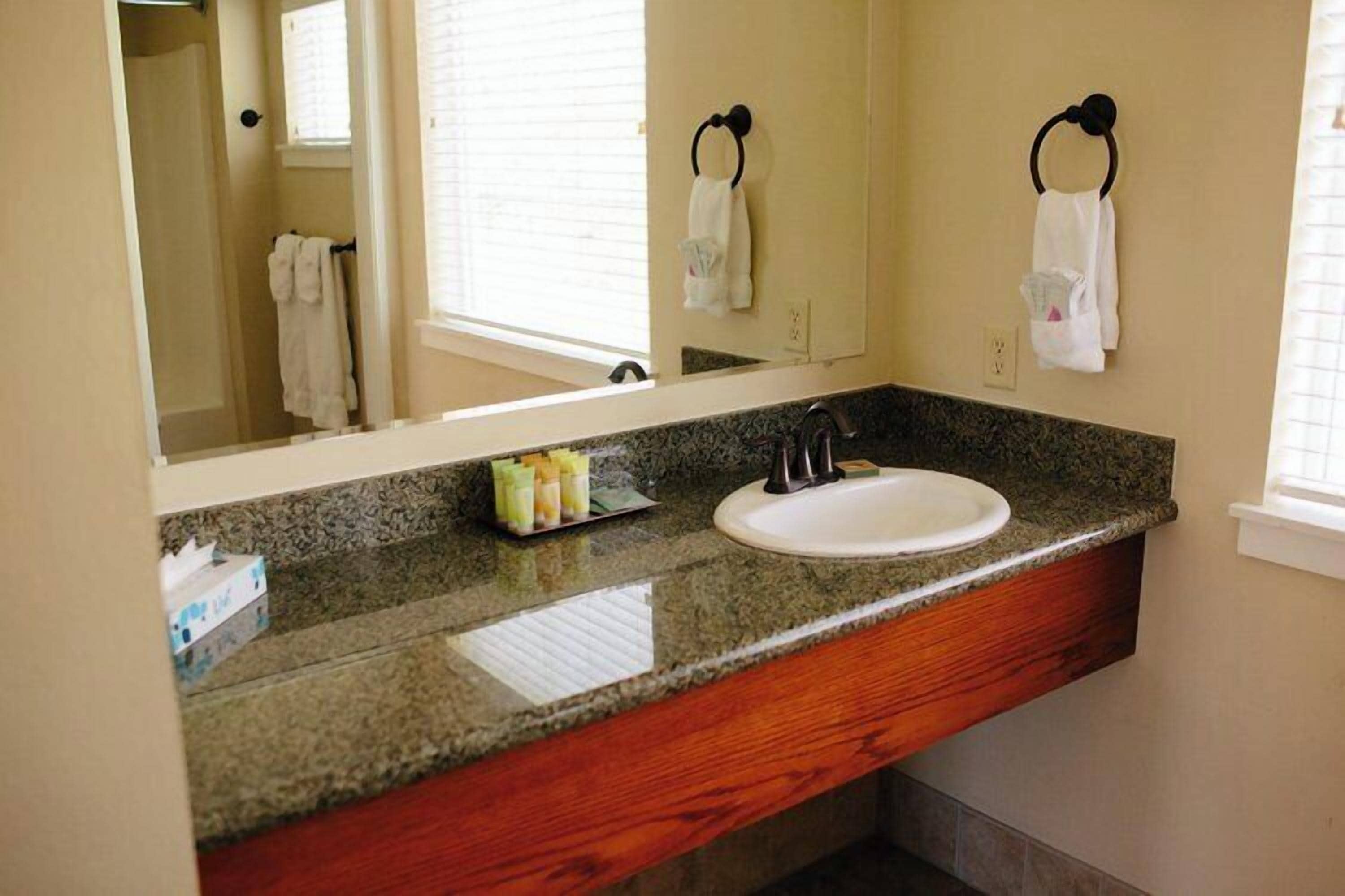 Un baño con encimera de granito, un lavabo blanco y un espejo grande.