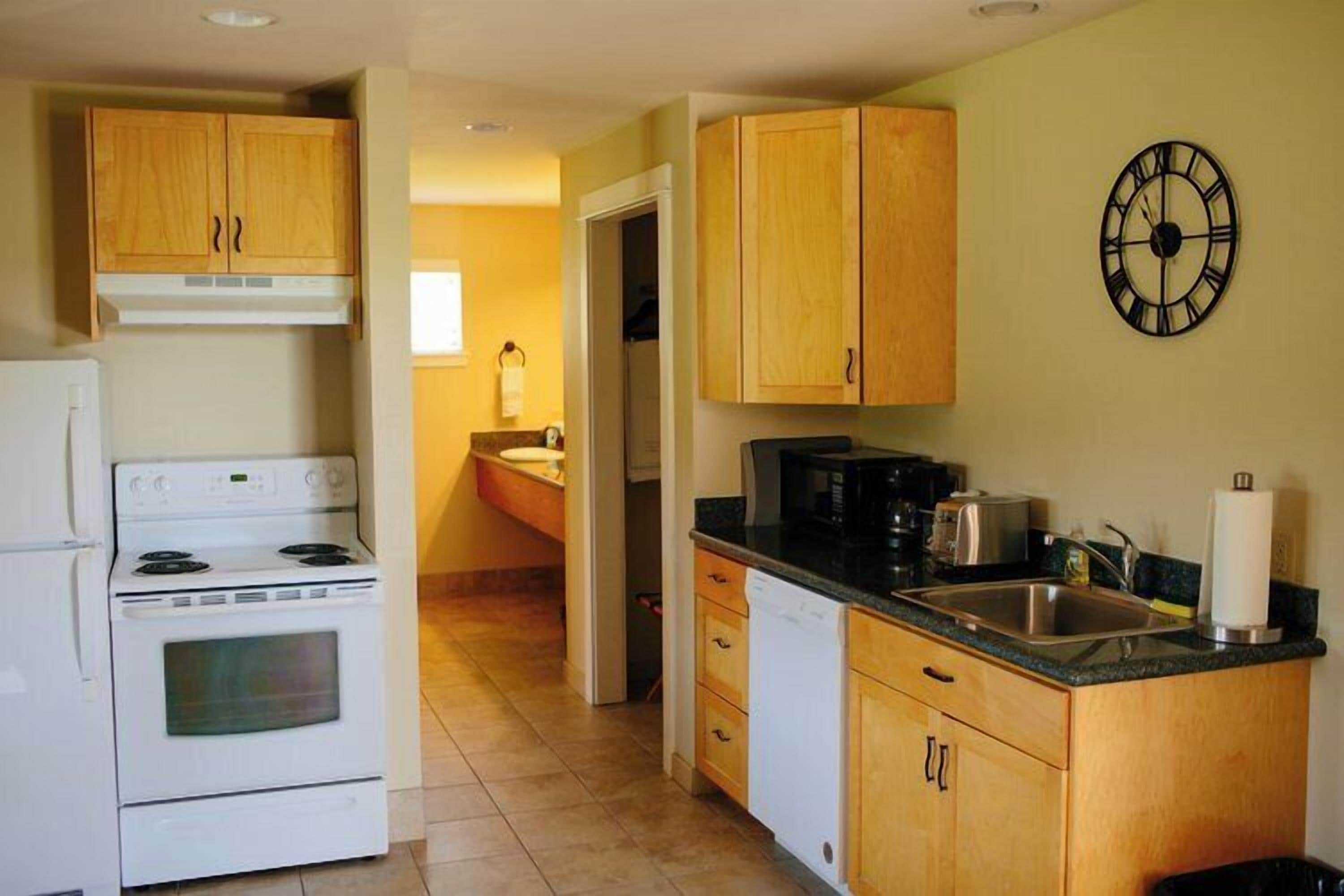 A kitchen with wooden cabinets, a white stove, a black microwave, and a sink.